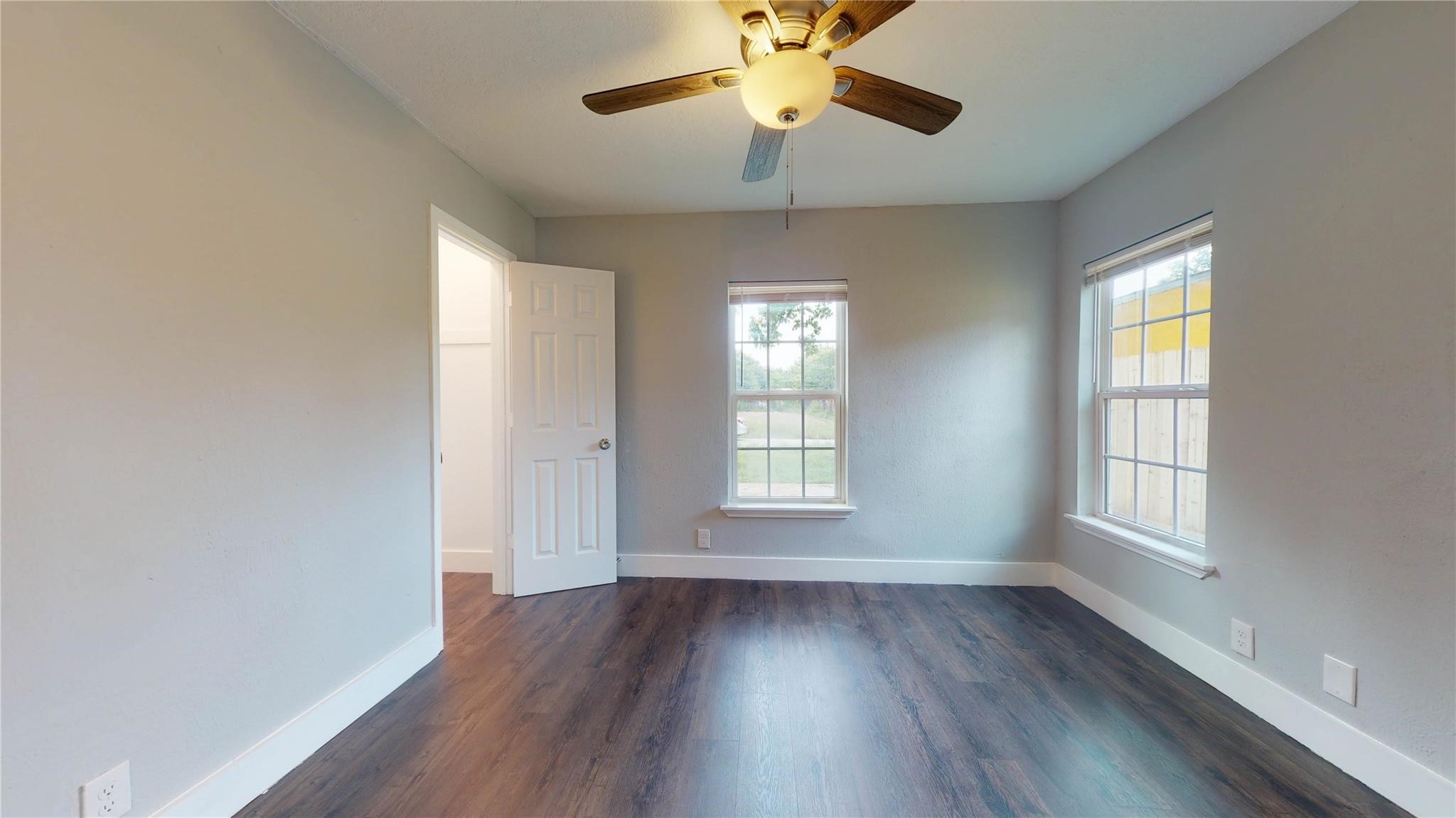 7346 Iwo Jima Road Houston, TX 77033 - Photo 12 of 20 This room features wood flooring, neutral walls, and ample natural light from two windows. A ceiling fan with a light fixture adds comfort, and there is a white door leading to another space.