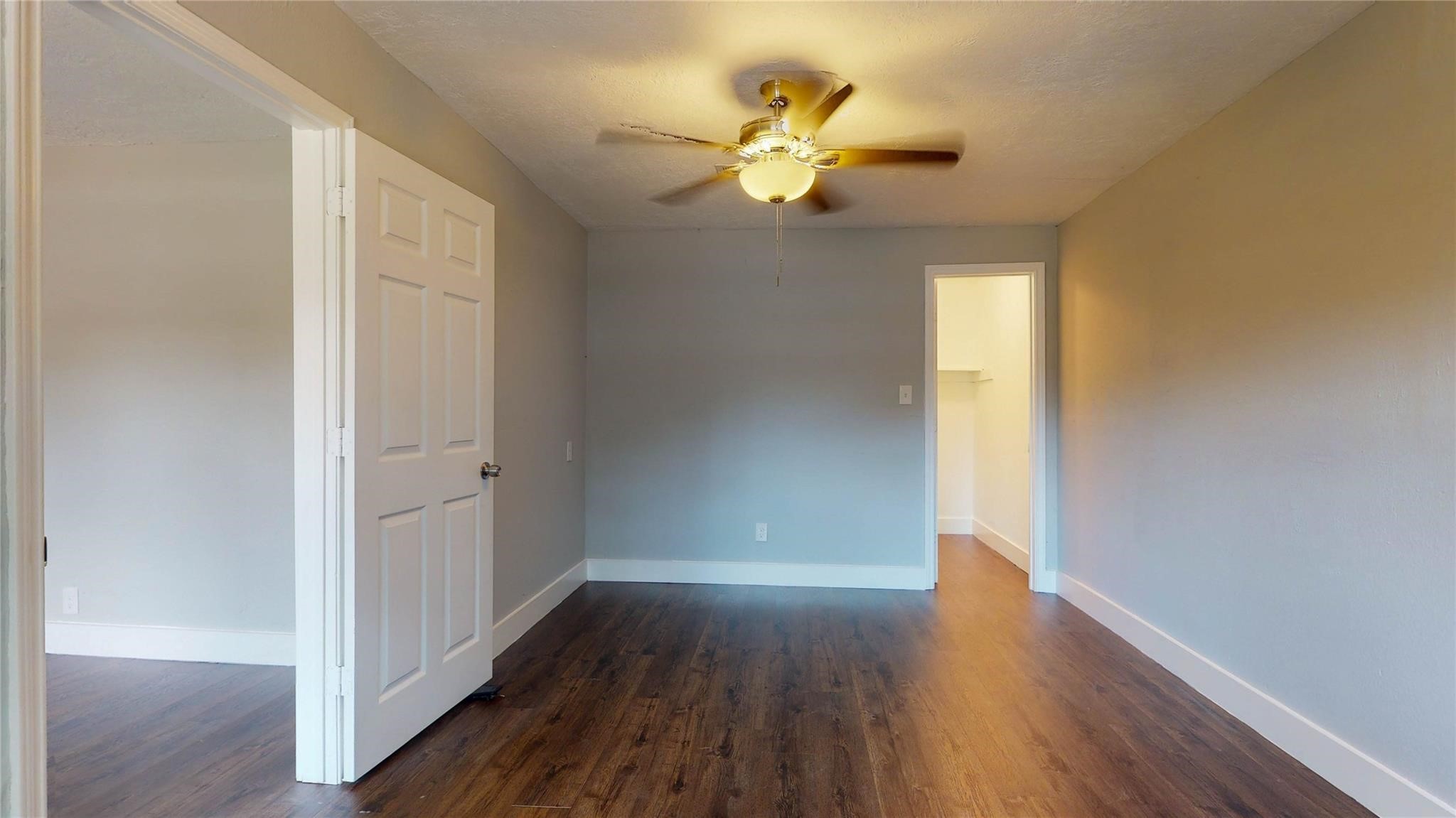 7346 Iwo Jima Road Houston, TX 77033 - Photo 17 of 20 This photo shows a bright, spacious bedroom with hardwood flooring and neutral-colored walls. It features a ceiling fan with a light fixture and has a walk-in closet visible through an open doorway. The room is well-lit and has a modern, clean look.