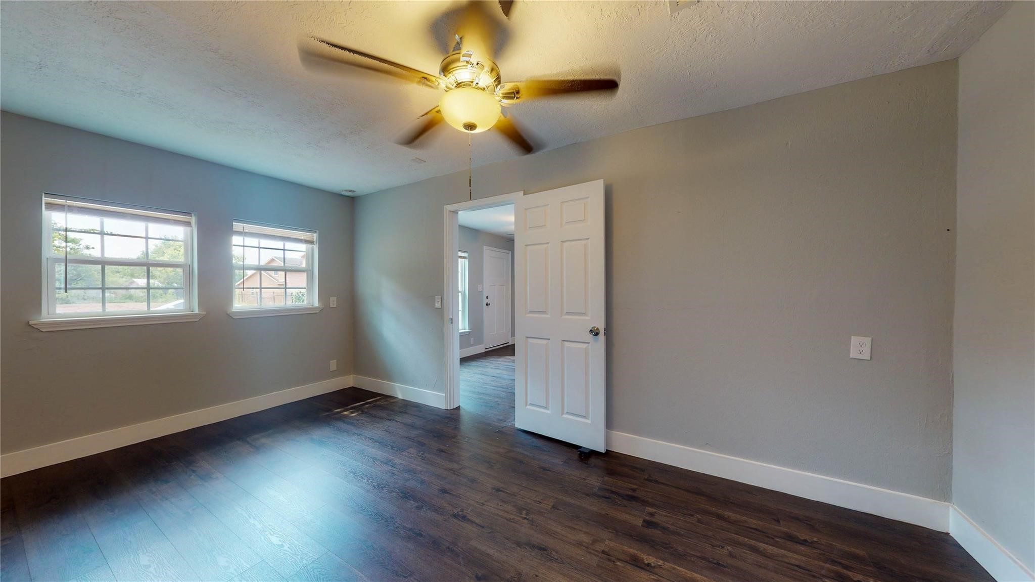 7346 Iwo Jima Road Houston, TX 77033 - Photo 18 of 20 This room features hardwood flooring, neutral gray walls, and two windows for natural light. A ceiling fan provides comfort, and an open door leads to the adjacent area, offering a welcoming and versatile space.