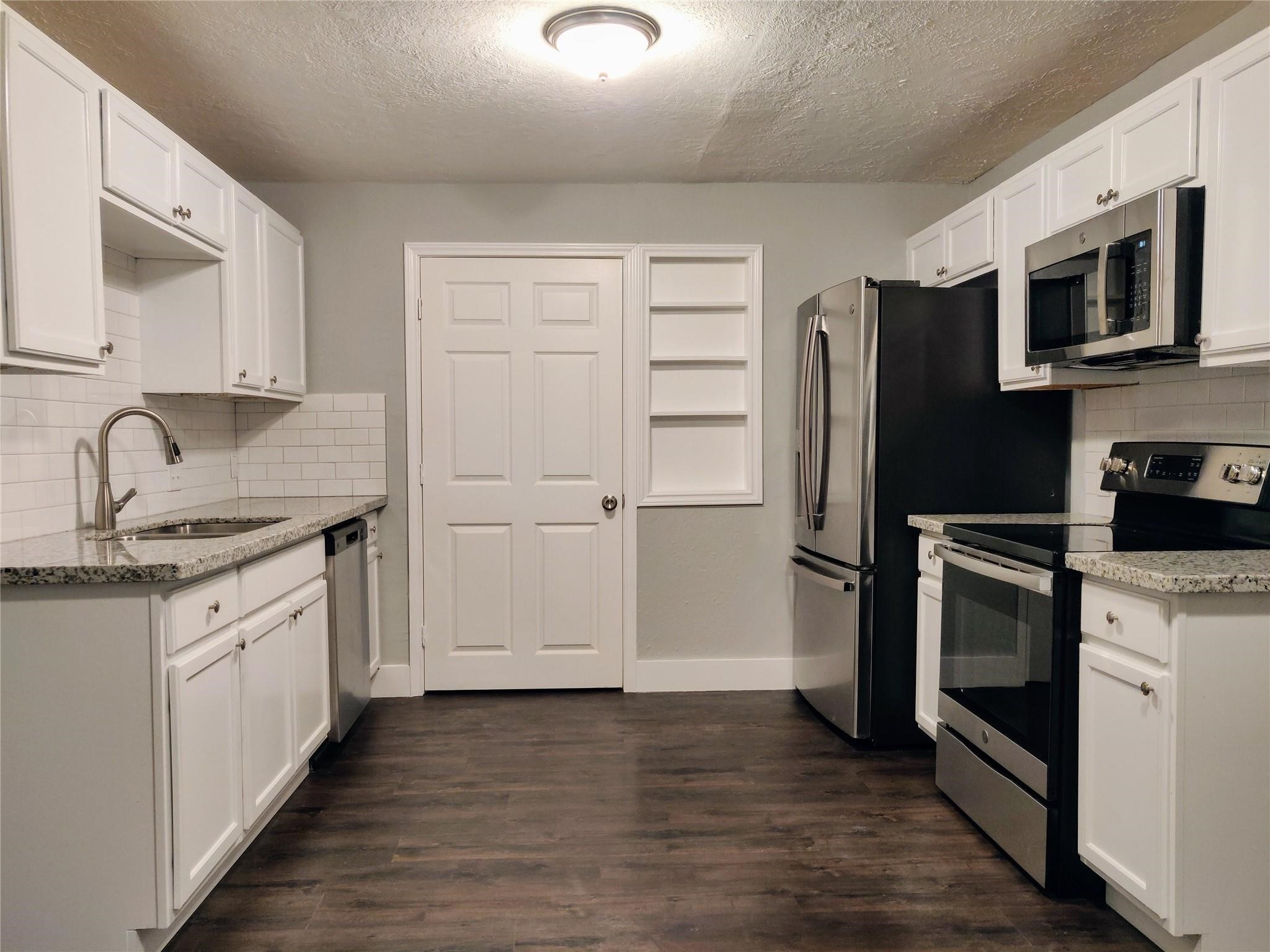 7346 Iwo Jima Road Houston, TX 77033 - Photo 3 of 20 This kitchen features modern stainless steel appliances, sleek granite countertops, and crisp white cabinetry. The dark hardwood floors add warmth, while a built-in shelf offers additional storage. Perfect for a contemporary home.