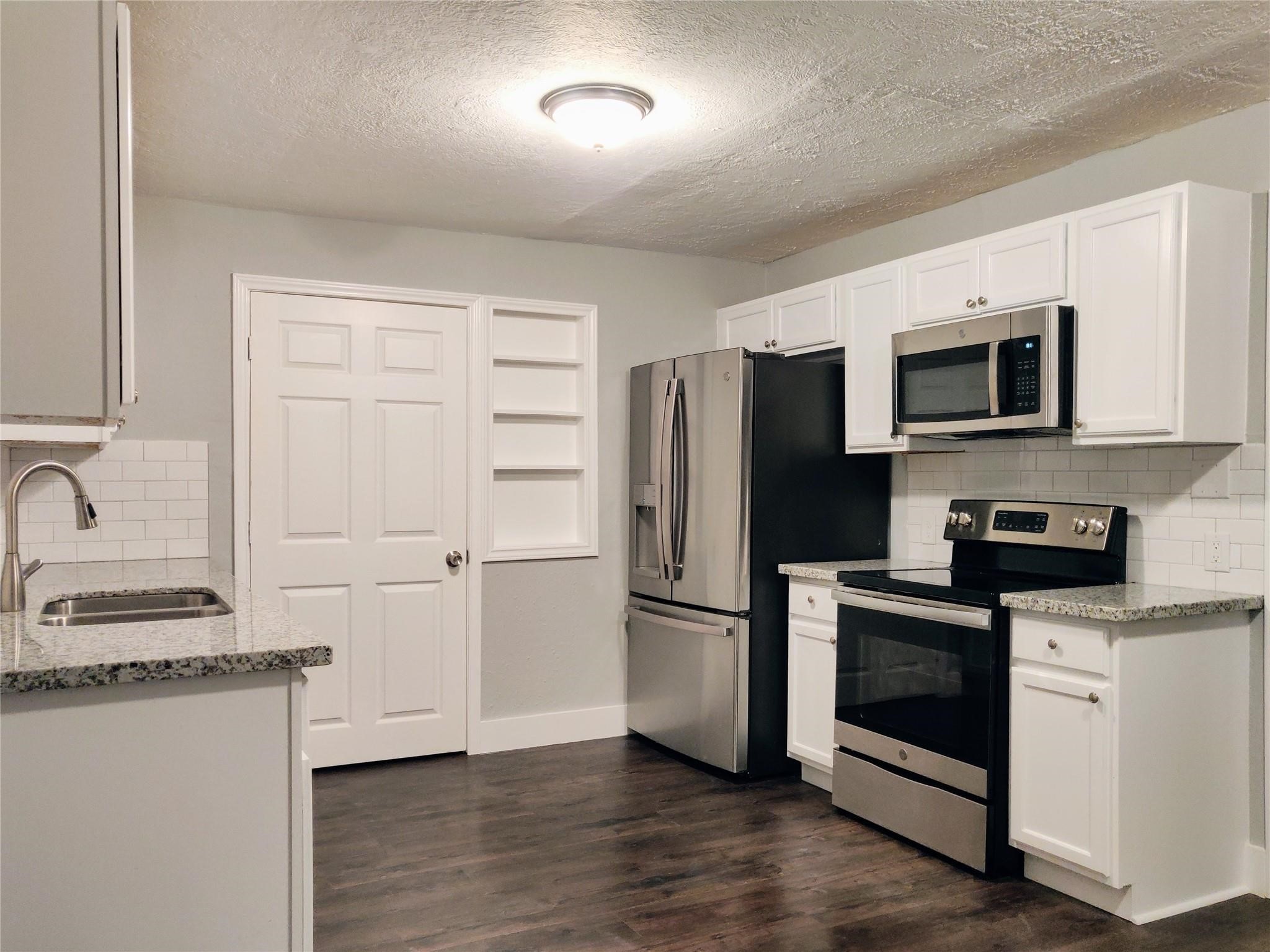 7346 Iwo Jima Road Houston, TX 77033 - Photo 4 of 20 This kitchen features modern stainless steel appliances, white cabinets, and granite countertops. It has a clean, contemporary look with a tiled backsplash and dark wood flooring, offering a functional and stylish space.