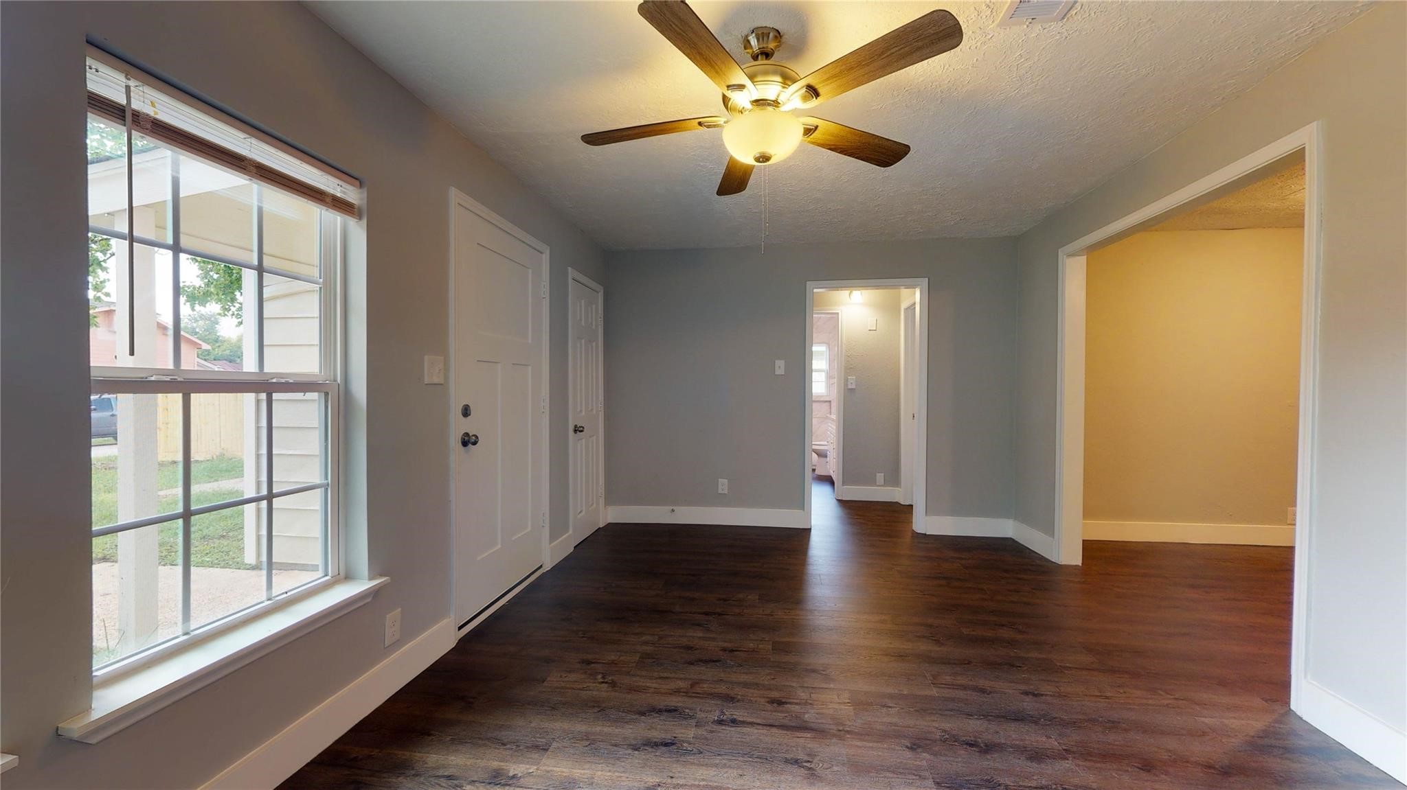 7346 Iwo Jima Road Houston, TX 77033 - Photo 9 of 20 This photo shows a bright living area with wood flooring, a large window, and a ceiling fan. The room features neutral gray walls and white trim, with visible doorways leading to other parts of the home.