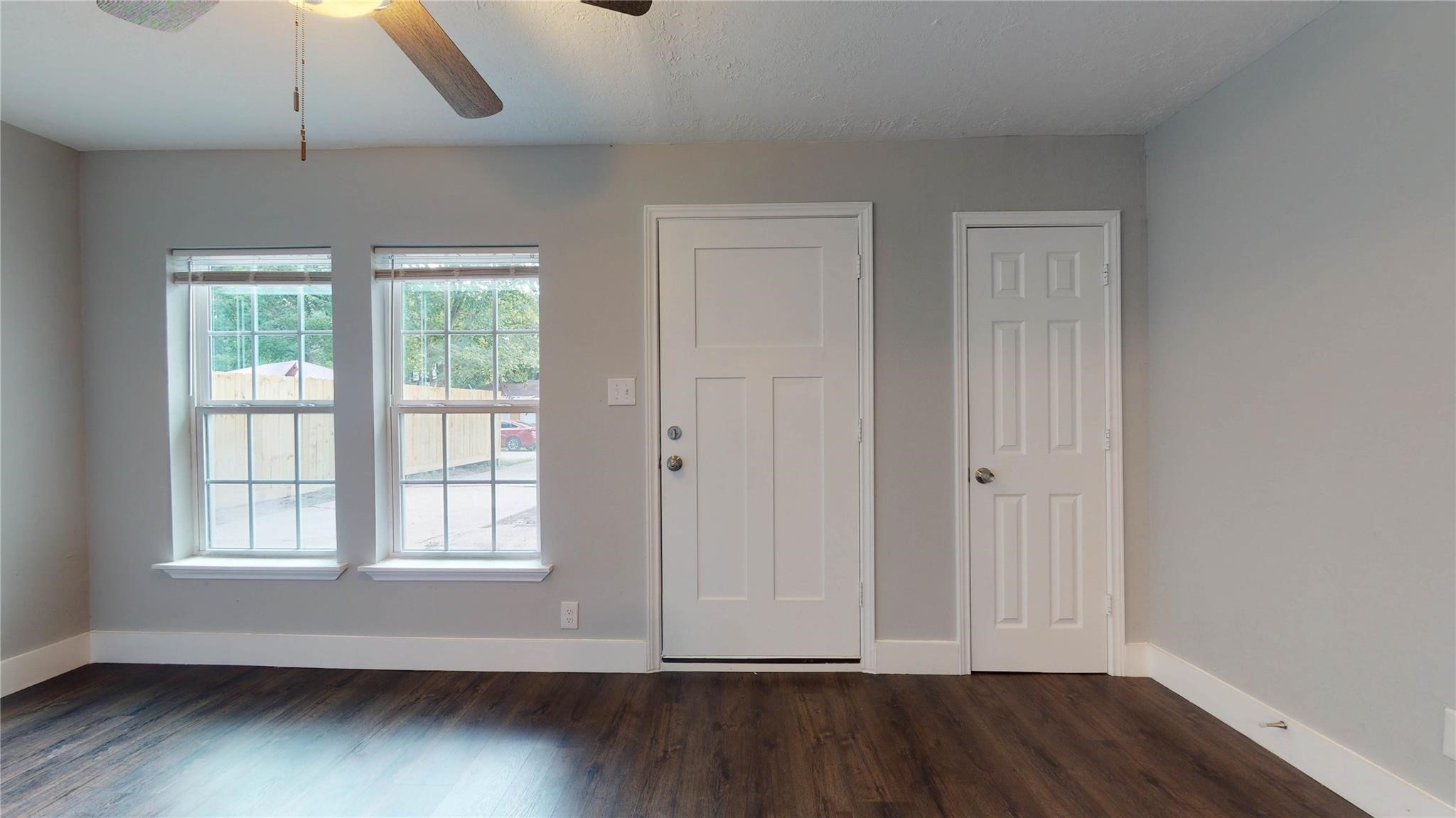 7346 Iwo Jima Road Houston, TX 77033 - Photo 10 of 20 Bright room with a modern feel, featuring two large windows for natural light, a ceiling fan, and dark wood flooring. The space includes a main door and an additional interior door, ideal for versatile use.