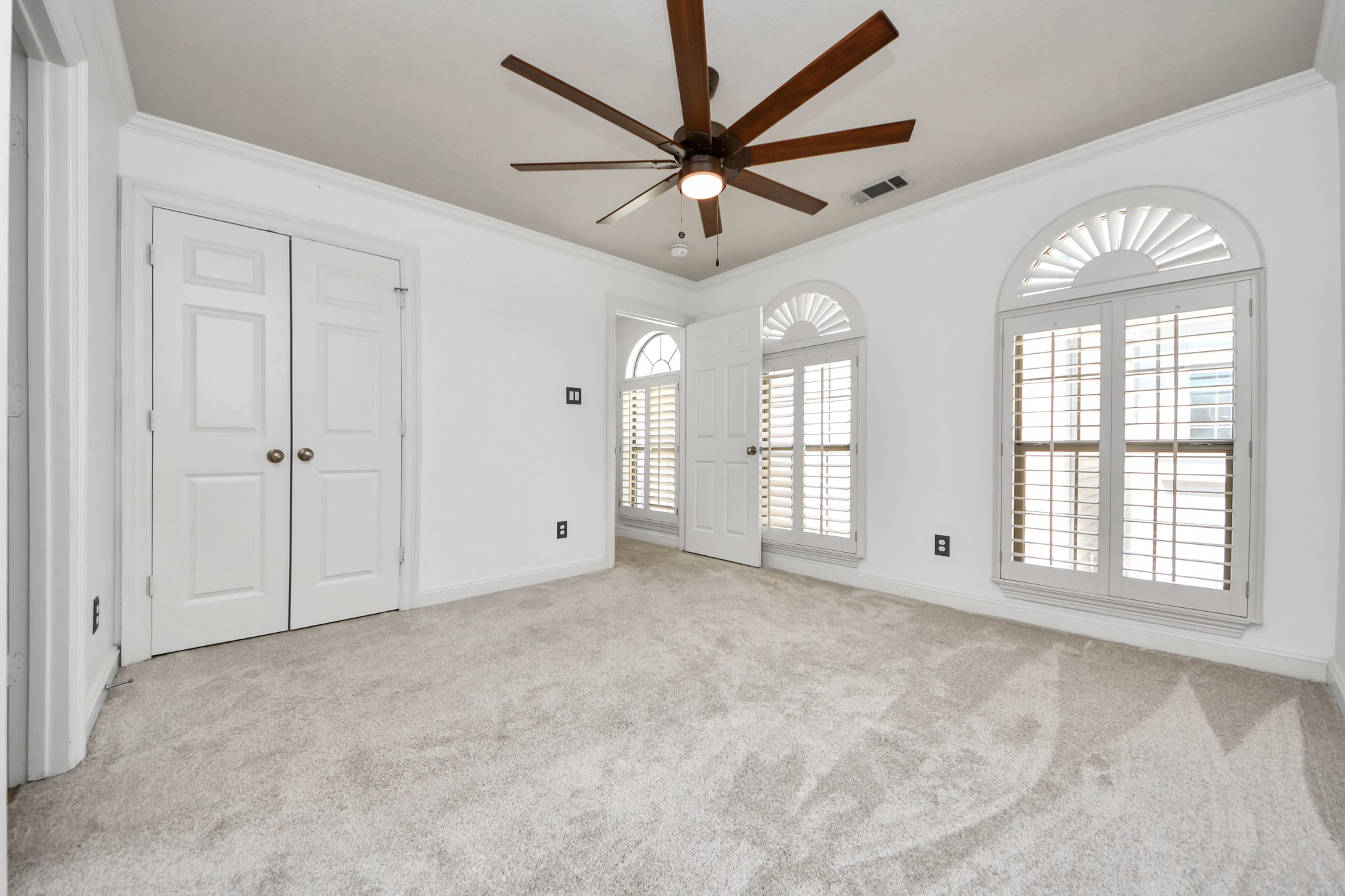 710 Jackson Hill Street Houston, TX 77007 - Photo 19 of 31 Secondary bedroom with arched windows and plantation shutters, featuring a ceiling fan and neutral carpet.