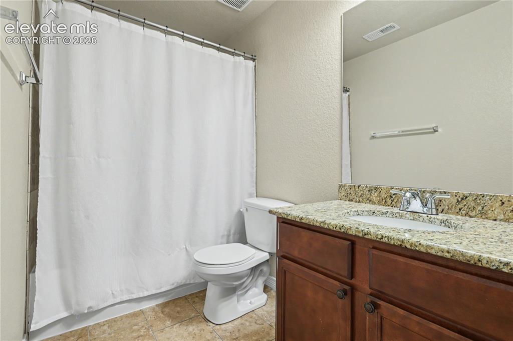 6598 Alliance Loop Colorado Springs, CO 80925 - Photo 31 of 39 Bathroom featuring a dark wood-finish vanity with a light-toned, speckled countertop, an undermount sink, and a chrome faucet