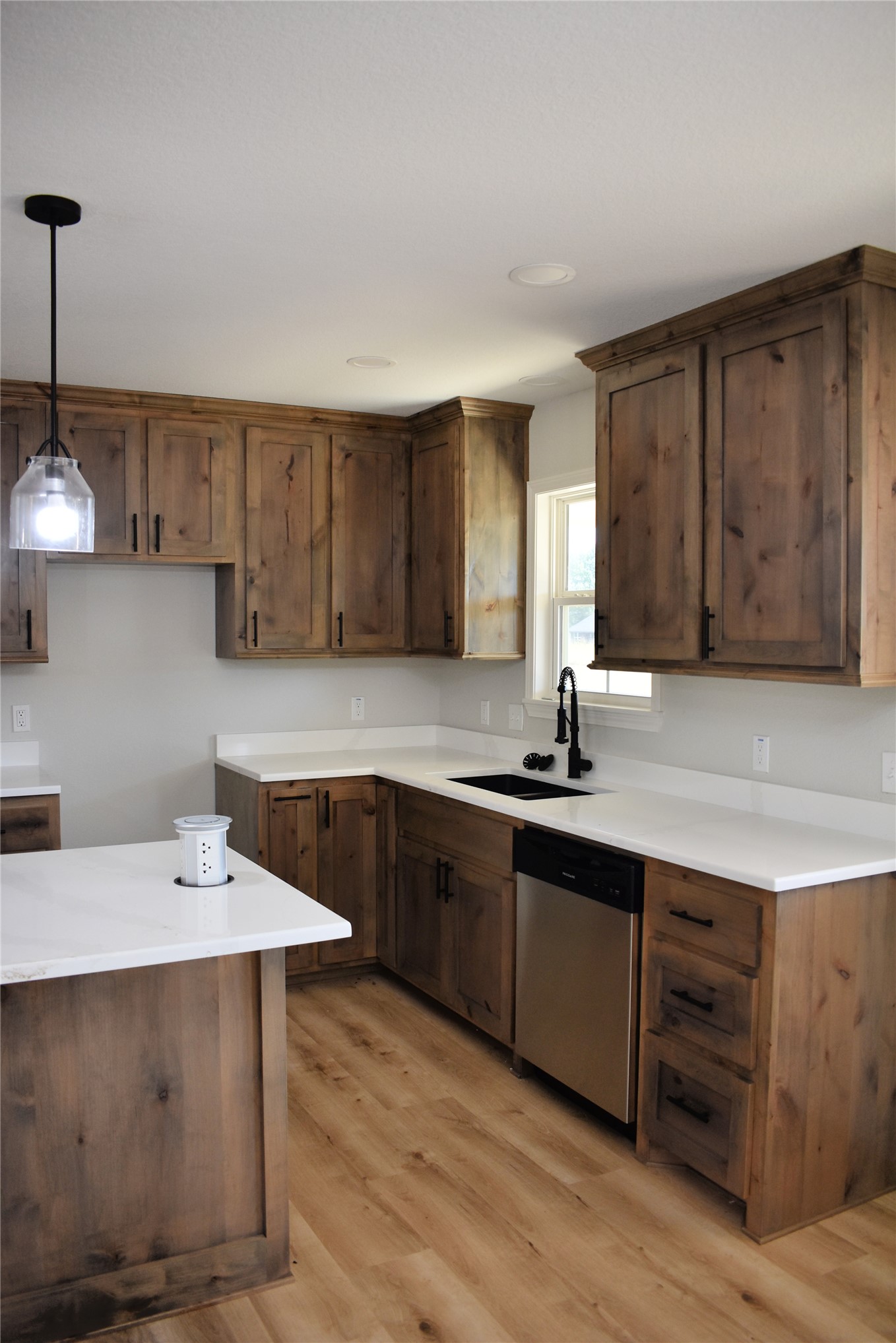 2911 East 2090 Road Hugo, OK 74743 - Photo 8 of 22 Wood-finish flooring, white countertops, dark wood cabinetry, black kitchen faucet, and a stainless steel dishwasher