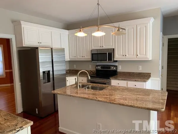 a kitchen with granite countertop a refrigerator a sink a stove a microwave and wooden cabinets