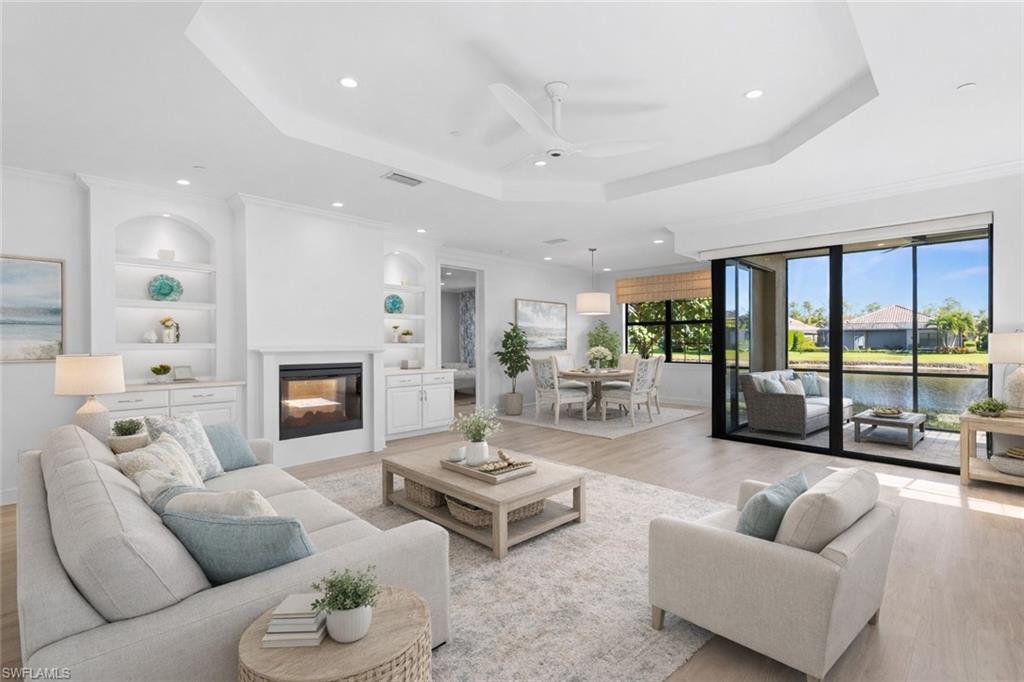 Living area featuring light wood finished floors, a ceiling fan, built in shelves, a glass covered fireplace, and a raised ceiling