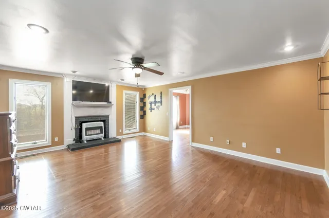 a view of a livingroom with a fireplace a ceiling fan and wooden floor