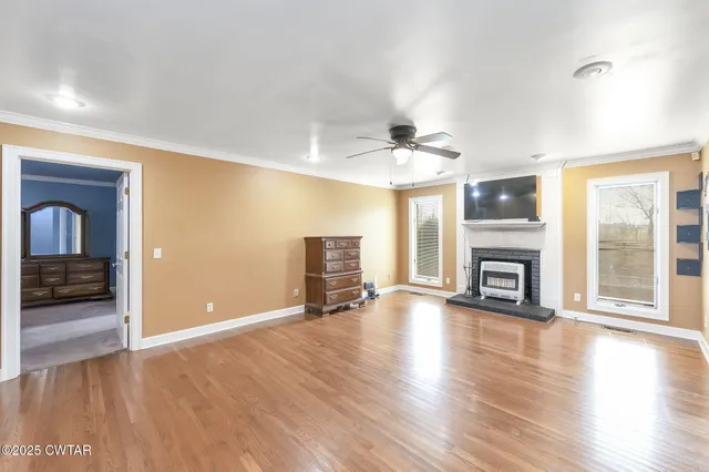 an empty room with wooden floor fireplace and windows