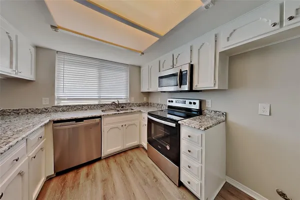 a kitchen with granite countertop a sink cabinets stainless steel appliances and a window