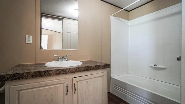 a bathroom with a granite countertop sink and mirror with bathtub