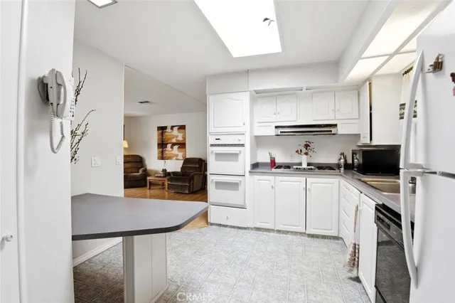 a kitchen with stainless steel appliances kitchen island granite countertop a refrigerator a sink a stove and white cabinets