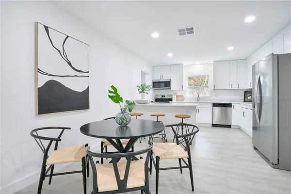 a kitchen with stainless steel appliances kitchen island granite countertop a dining table chairs and a refrigerator