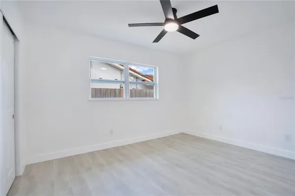 an empty room with wooden floor ceiling fan and window