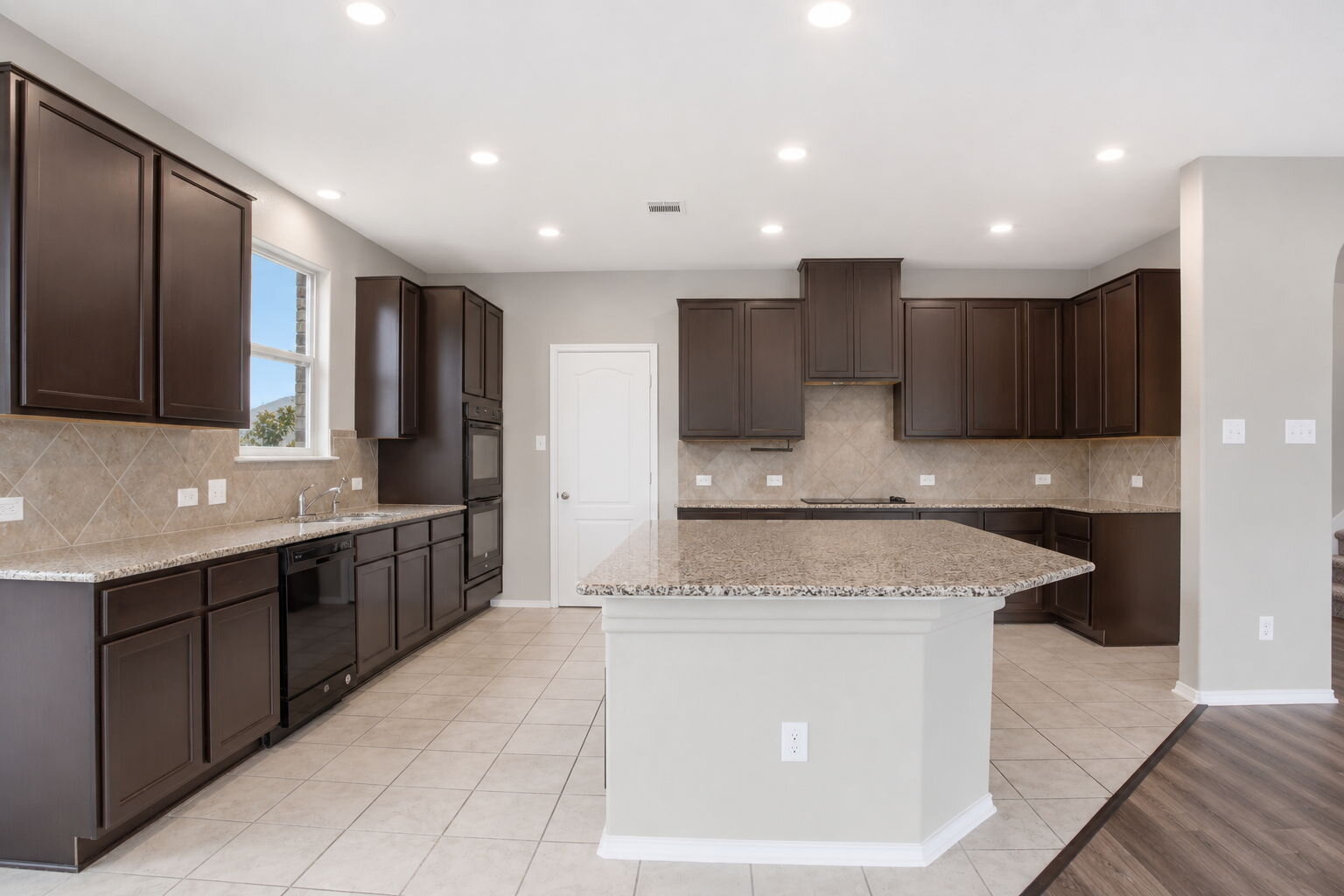 670 Landon Samuel Loop Pflugerville, TX 78660 - Photo 4 of 22 Spacious kitchen featuring dark wood cabinetry, light granite countertops, a tiled backsplash, and an expansive kitchen island