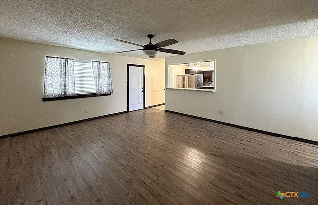 an empty room with wooden floor chandelier fan and windows