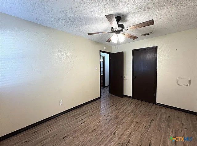 an empty room with wooden floor fan and windows