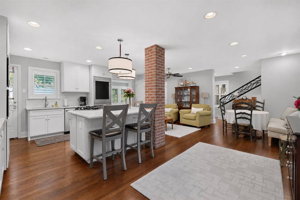 4548 Roland Avenue, Unit A Dallas, TX 75219 - Photo 7 of 31 Hardwood flooring throughout, white cabinetry with integrated appliances, kitchen island with seating, recessed lighting, and a brick-faced structural column