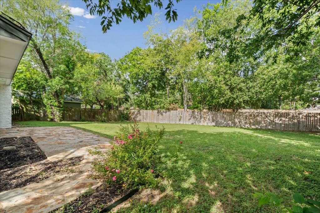 1406 North Georgetown Street Round Rock, TX 78664 - Photo 29 of 34 A stone patio transitions to a lush, green yard bordered by a privacy fence and mature trees.