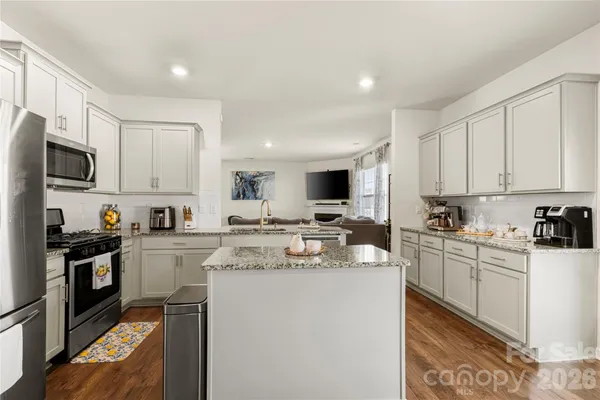 a kitchen with stainless steel appliances granite countertop a stove top oven a sink a refrigerator and white cabinets