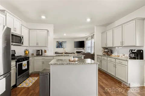 a kitchen with stainless steel appliances granite countertop a stove top oven a sink a refrigerator and white cabinets
