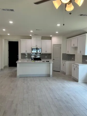 a large white kitchen with stainless steel appliances granite countertop a stove a sink a refrigerator and white cabinets with wooden floor