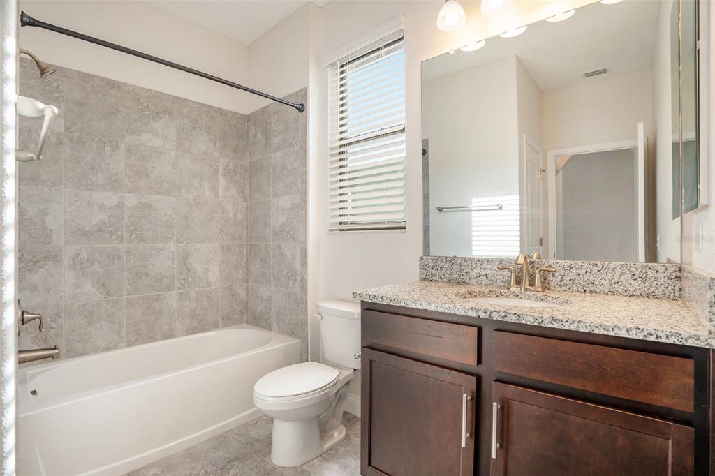12330 Newt Court New Port Richey, FL 34654 - Photo 26 of 30 a bathroom with a granite countertop sink a toilet a mirror a bathtub and shower
