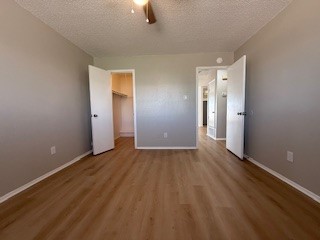 2202 Donahue Lane, Unit B Austin, TX 78744 - Photo 11 of 16 Unfurnished bedroom with a walk in closet, light wood-style flooring, a textured ceiling, and a ceiling fan