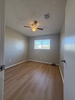 2202 Donahue Lane, Unit B Austin, TX 78744 - Photo 13 of 16 Empty room featuring a textured ceiling, light wood-type flooring, and a ceiling fan