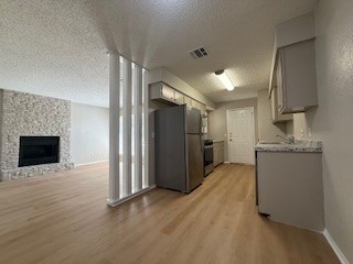2202 Donahue Lane, Unit B Austin, TX 78744 - Photo 5 of 16 Kitchen featuring a textured ceiling, freestanding refrigerator, light wood-style floors, a fireplace, and light countertops