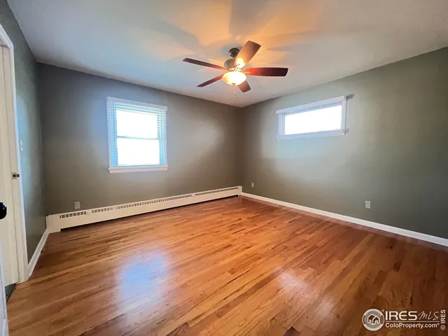 an empty room with wooden floor chandelier fan and windows