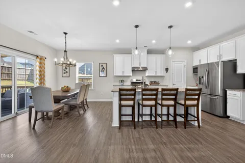a kitchen with stainless steel appliances a dining table chairs stove refrigerator and cabinets