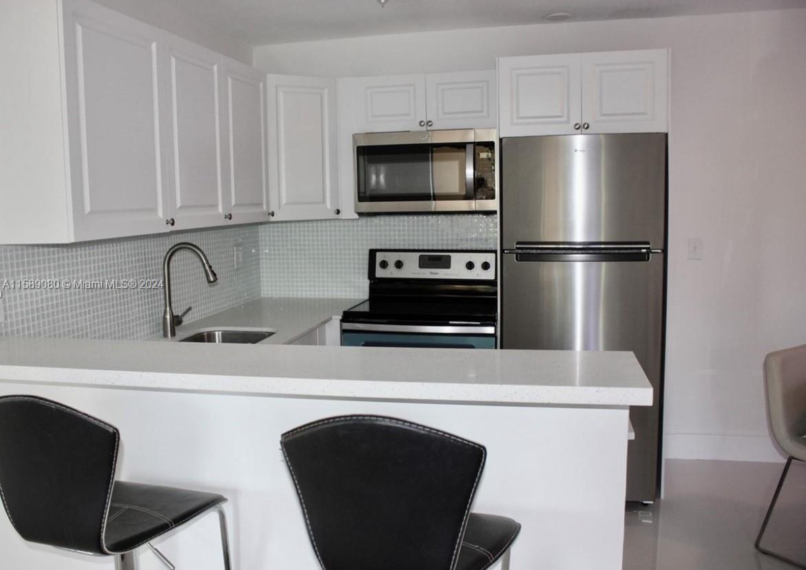 a kitchen with stainless steel appliances a refrigerator a sink a stove and white cabinets