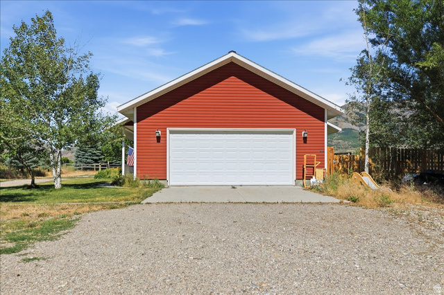 1634 West Arimo Road Arimo, ID 83214 - Photo 30 of 89 Red horizontal siding exterior with a white garage door, concrete driveway apron, and a gravel surface