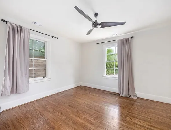 an empty room with wooden floor fan and windows