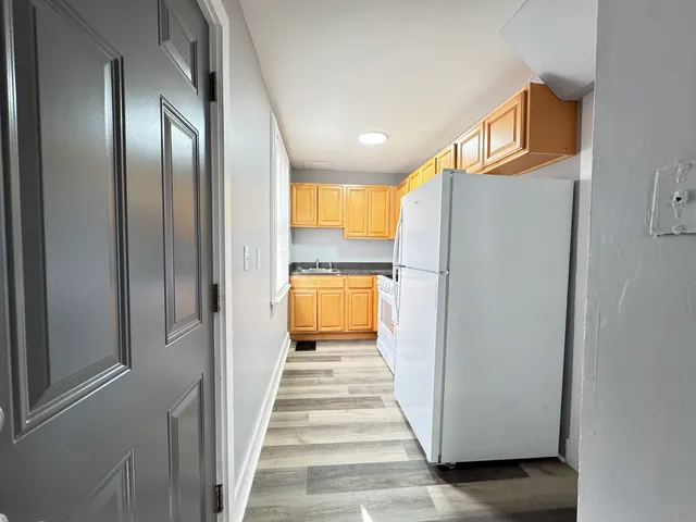 a view of a hallway with wooden floor and a kitchen