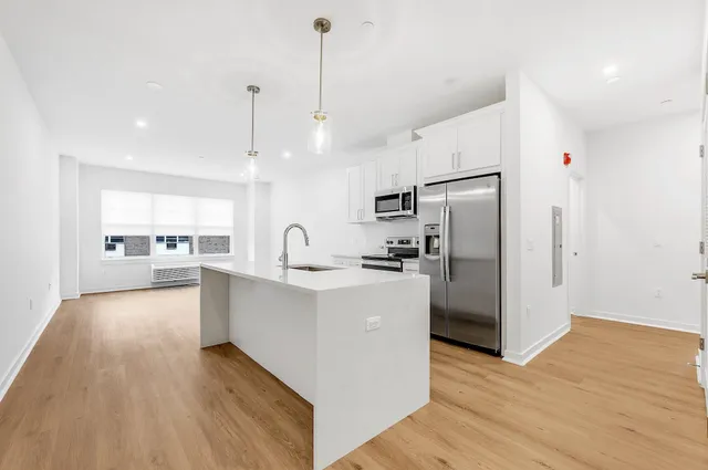 a large kitchen with stainless steel appliances a refrigerator a sink dishwasher a oven and white cabinets with wooden floor