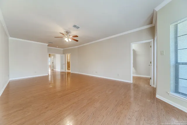 a view of an empty room with wooden floor and a ceiling fan