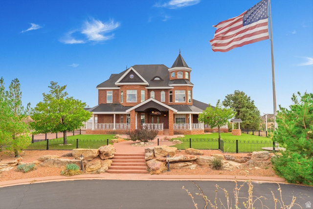 Victorian home with a porch, brick siding, and a fenced front yard