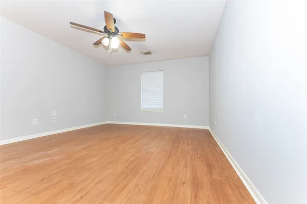 an empty room with wooden floor fan and windows