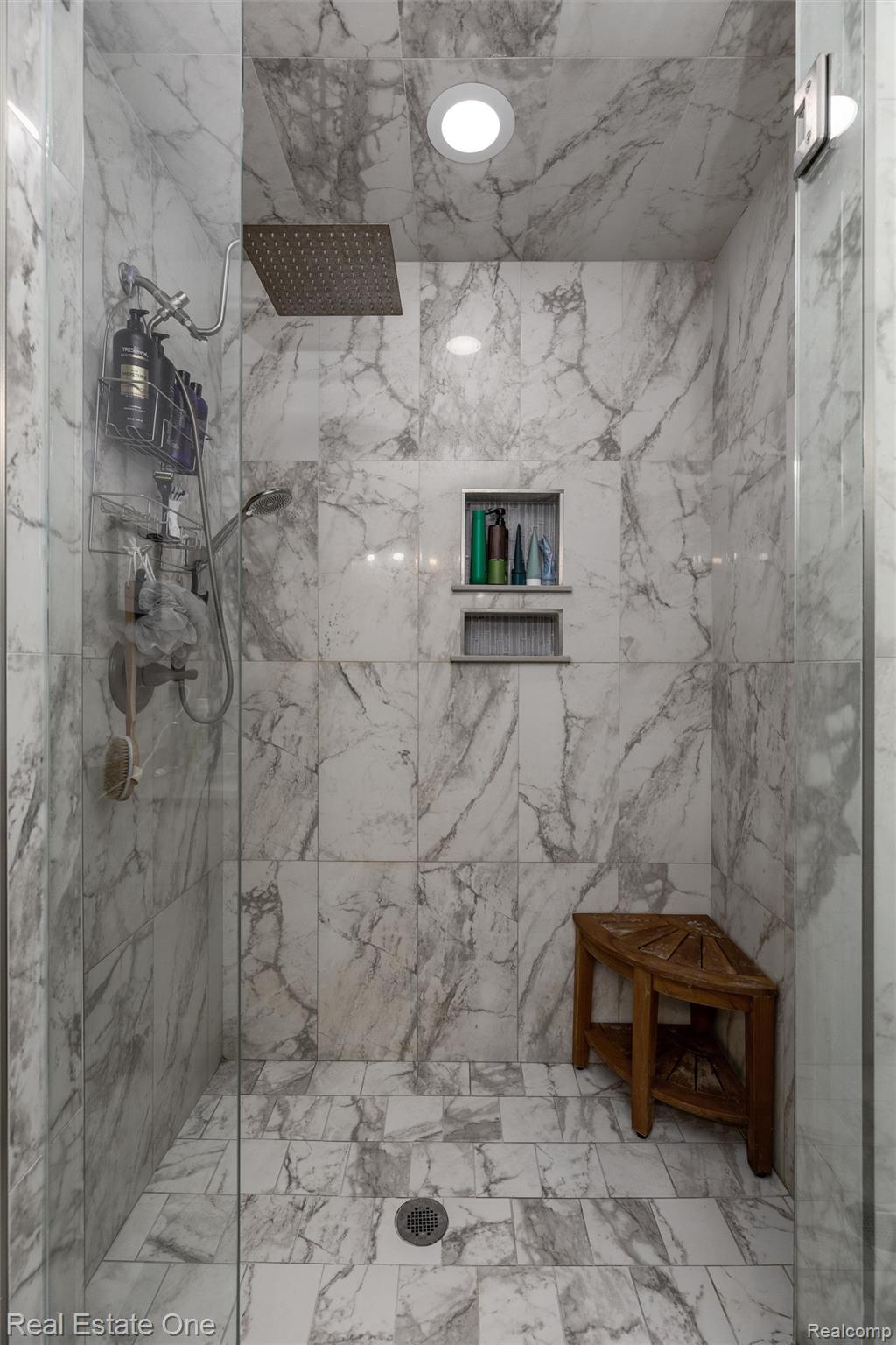 2983 28 Mile Road Washington, MI 48094 - Photo 30 of 54 Walk-in shower featuring full-height marble-patterned tile, a recessed niche with shelving, and a rain shower head with an additional handheld sprayer