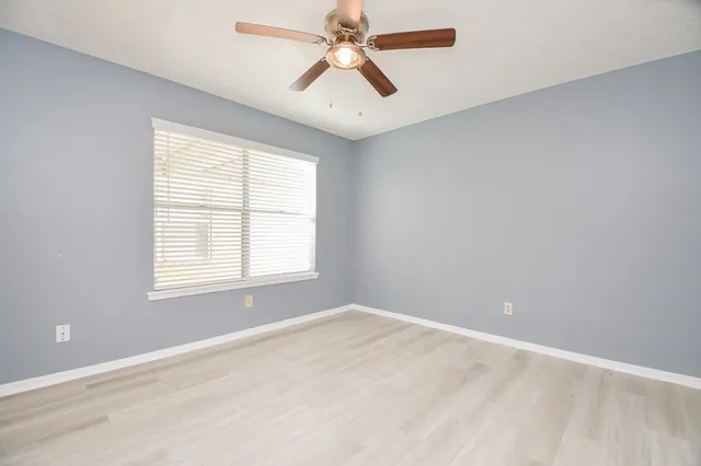 an empty room with chandelier fan and windows