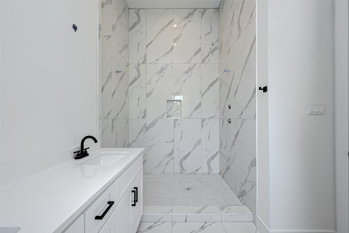 6032 Beall Street Houston, TX 77091 - Photo 19 of 26 The spa-inspired walk-in shower is wrapped in elegant porcelain tile with dramatic veining, offering a luxurious retreat in the primary en-suite bathroom.