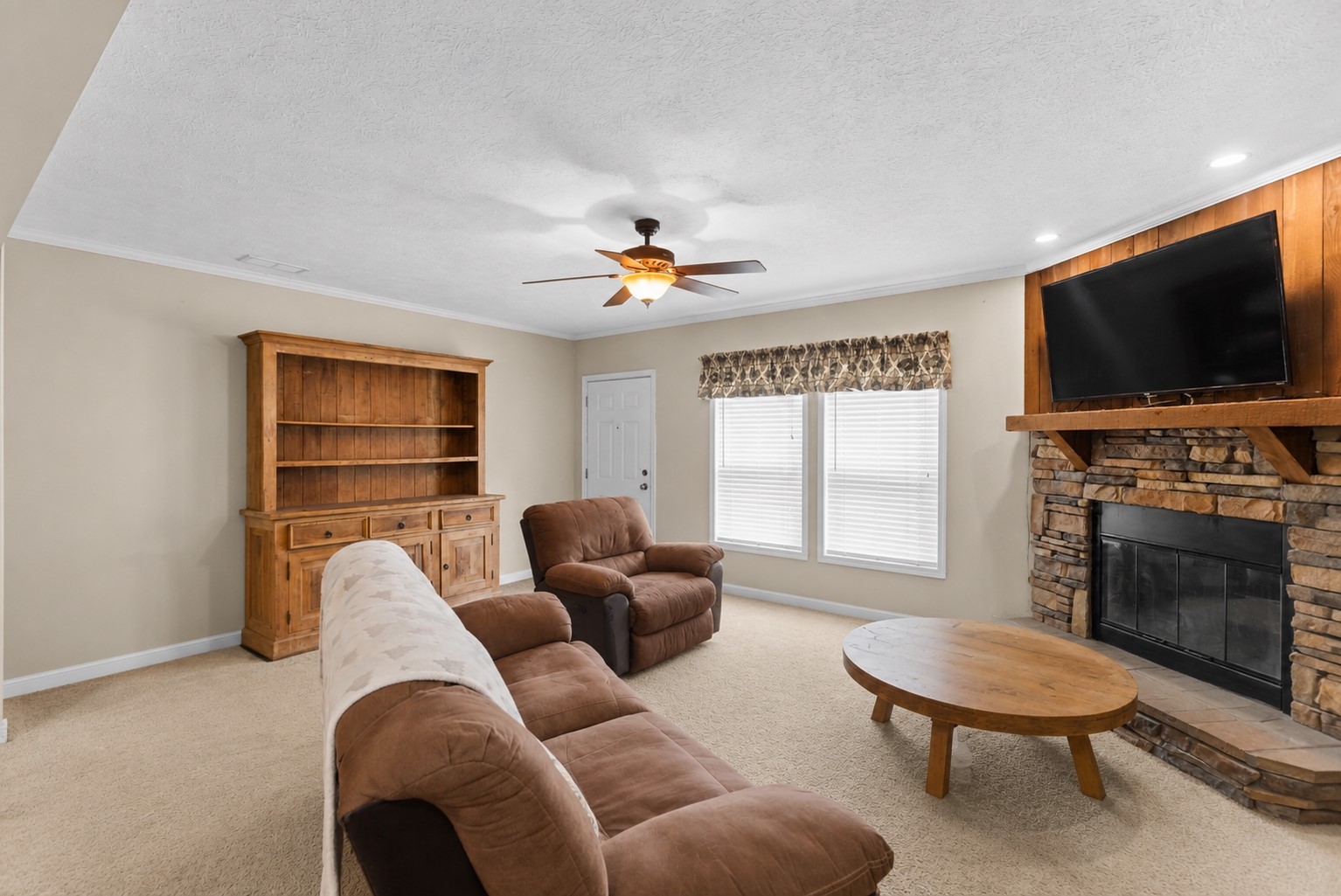 1800 2110th Road Hugo, OK 74743 - Photo 6 of 27 Stone-clad fireplace with wood mantel, multiple windows, and a ceiling fan with integrated lighting