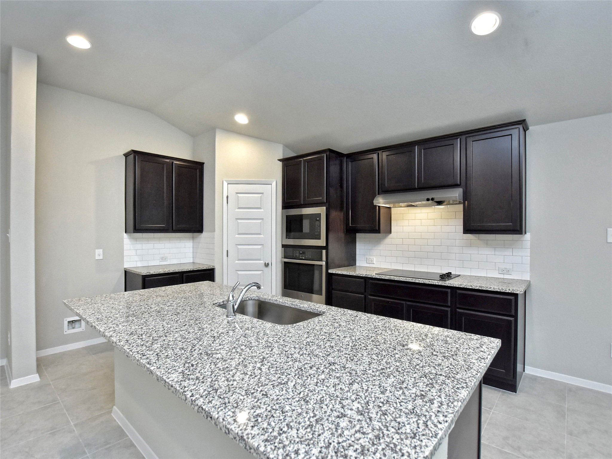 20701 Boggy Ford Road Lago Vista, TX 78645 - Photo 10 of 40 Kitchen featuring light stone counters, stainless steel appliances, backsplash, a center island with sink, and dark wood finish cabinets