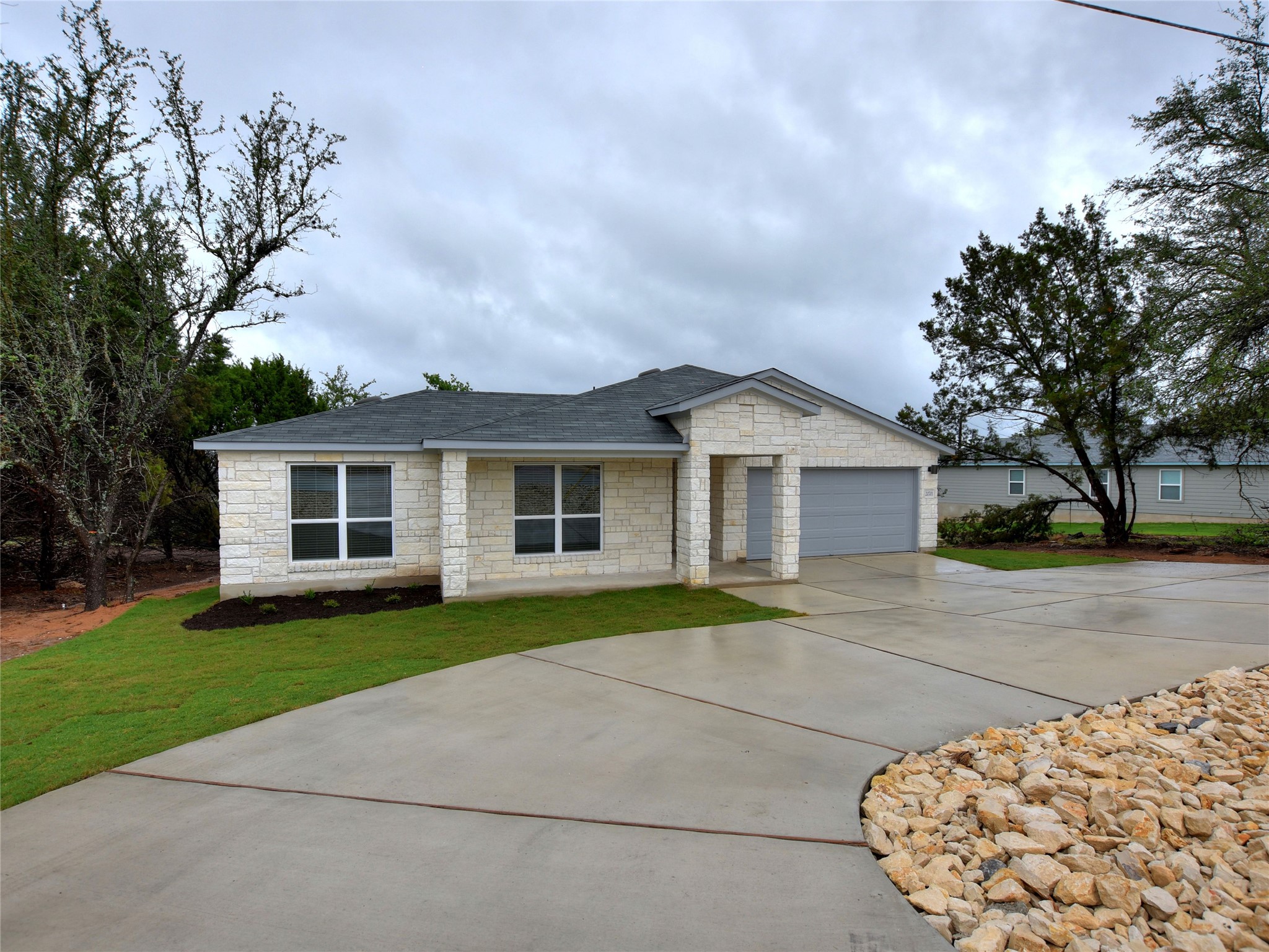 20701 Boggy Ford Road Lago Vista, TX 78645 - Photo 4 of 40 Ranch-style house featuring stone siding, a front lawn, concrete driveway, roof with shingles, and an attached garage