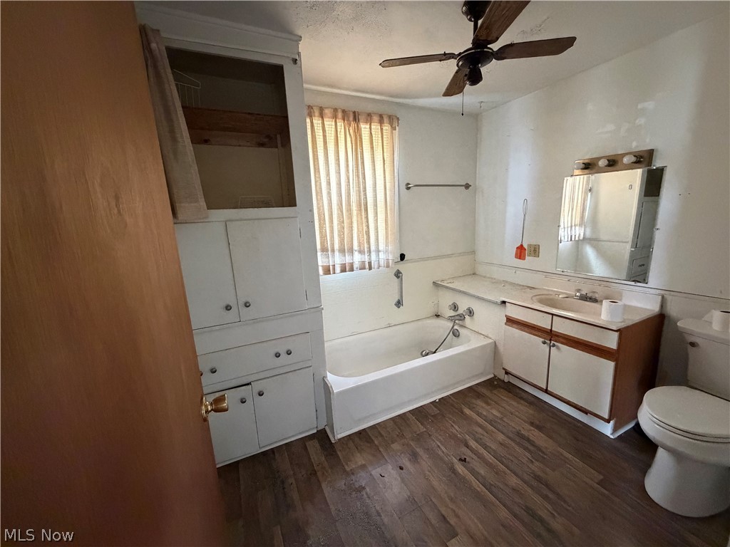 32 Cherry Road Northwest Massillon, OH 44646 - Photo 11 of 12 Bathroom featuring wood-finish flooring, a built-in vanity with sink, a white bathtub, and an integrated storage cabinet with glass accents