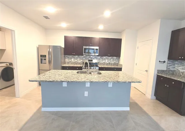 a view of kitchen island with stainless steel appliances granite countertop wooden cabinets and a sink