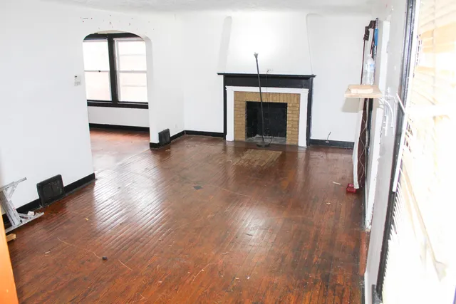 an empty room with wooden floor fireplace and windows